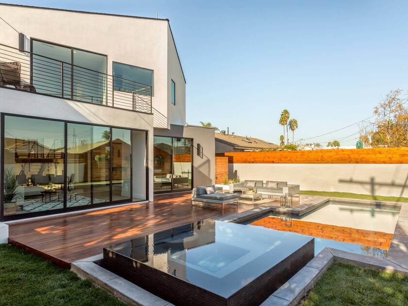 Modern Los Angeles home with large glass doors, wood deck, outdoor seating, and a backyard pool.