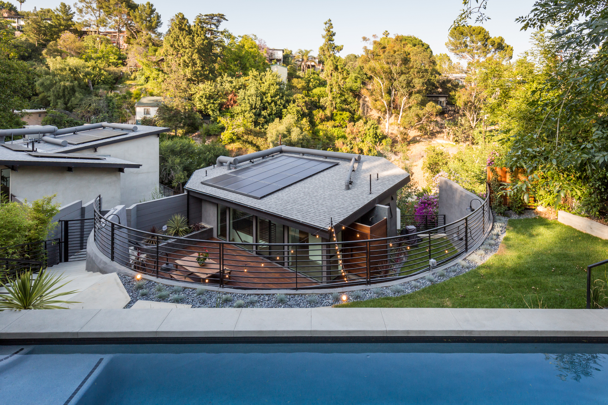 Terraced backyard of a modern Northeast Los Angeles hillside home with a pool, curved metal railings, outdoor living spaces, and lush hillside landscaping. Terraced backyard of a modern Northeast Los Angeles hillside home with a pool, curved metal railings, outdoor living spaces, and lush hillside landscaping.